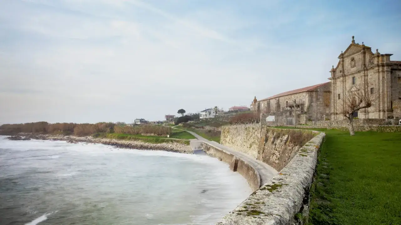 Monasterio de Santa María de Oia, con el mar agitado a la izquierda y un camino costero.