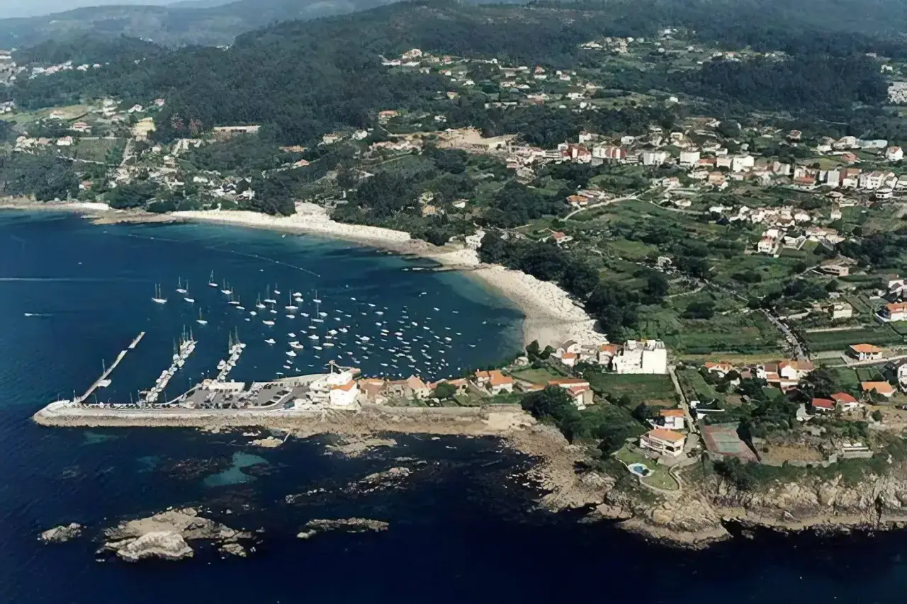 Vista aérea de la playa de Aguete con un puerto deportivo lleno de veleros, casas blancas y verdes colinas.