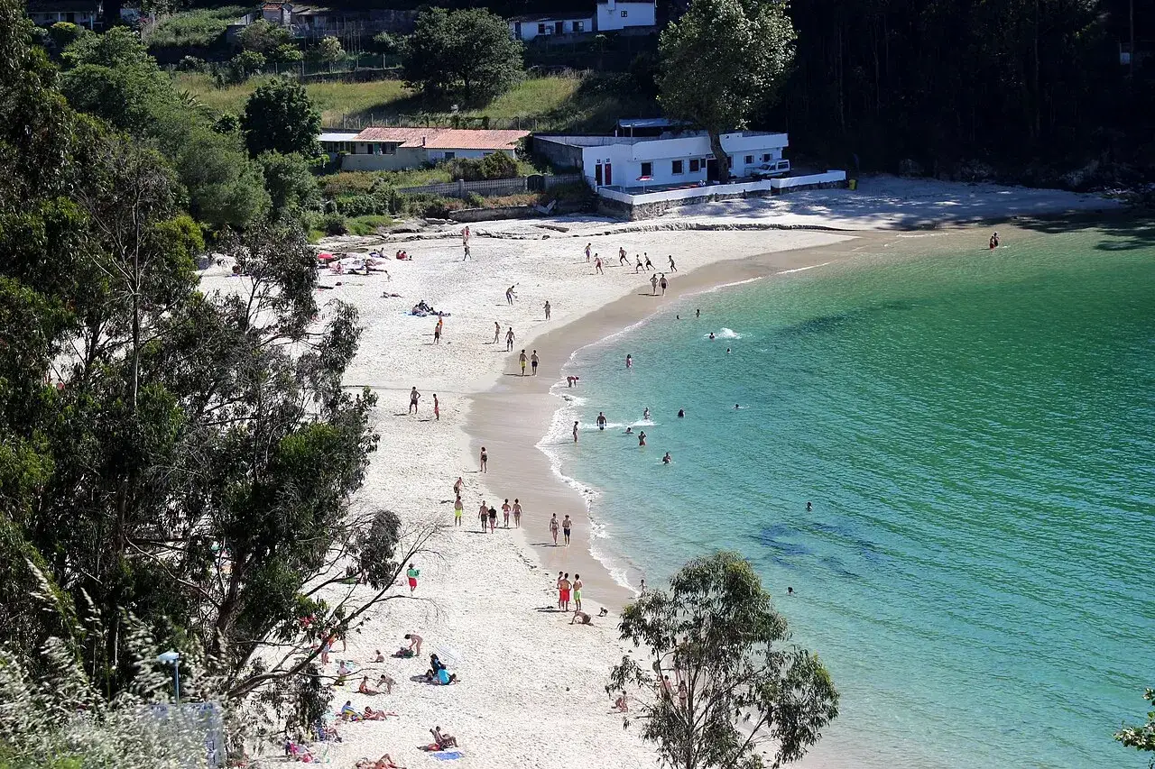 Gente disfrutando del sol y el mar en la playa Mogor, con aguas cristalinas y arena dorada.